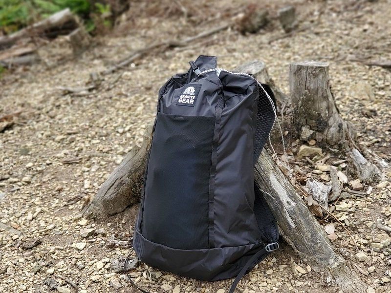 Ultralehký batoh na jednodenní výlety Granite Gear Sawbill 20 opřený v lese o kmen.
