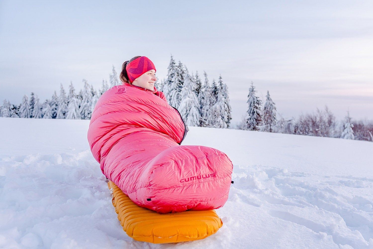 Osoba ve spacáku Cumulus Panyam 450 v červené barvě při kempování na sněhu na nafukovací karimatce