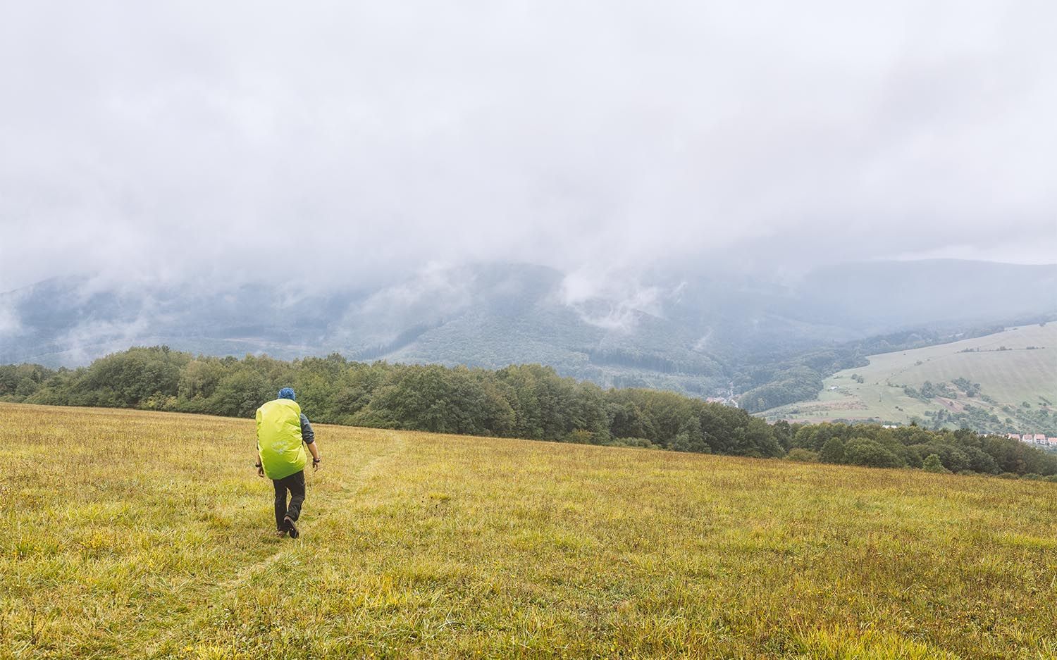 Osoba jdoucí přírodou s ultralehkým batohem potažený pláštěnkou.
