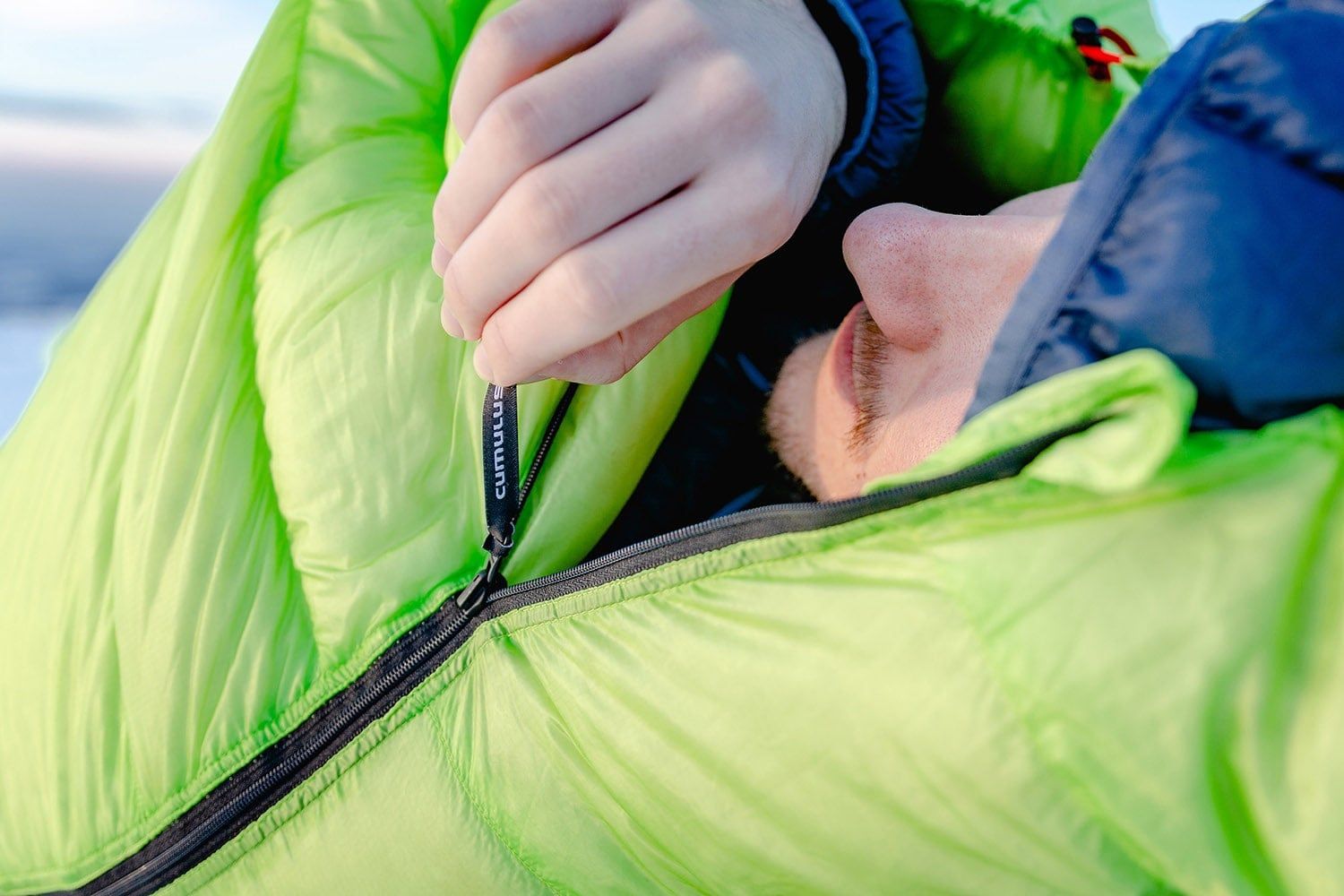 Osoba ležící v péřovém spacáku Cumulus X-Lite 400 v zelené barvě.